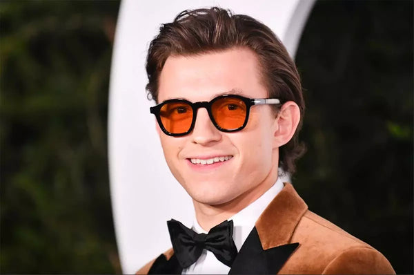 Person wearing sunglasses and a brown coat with a black bow tie, standing against a blurred background.